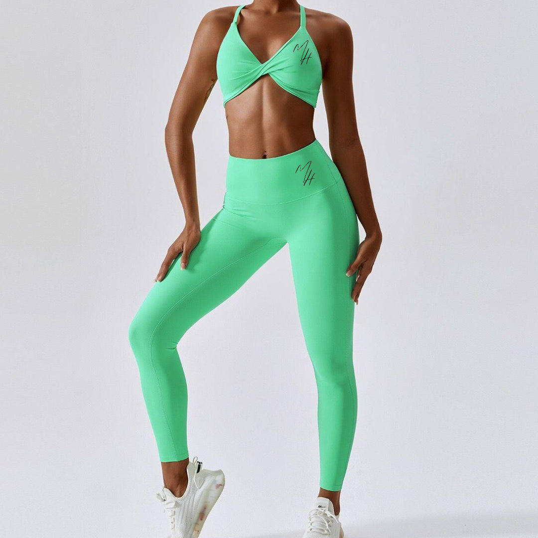 A photo of a woman wearing a stylish green 'BeYouAppleBottom' Crop Top paired with matching leggings, showcasing the epitome of style and functionality in activewear. The crop top features a flattering silhouette with the brand's iconic logo displayed on both front and back, while boasting padding for added support and a chic twist-hole design. This versatile ensemble transitions seamlessly from gym sessions to beach outings, embodying empowerment and self-expression.