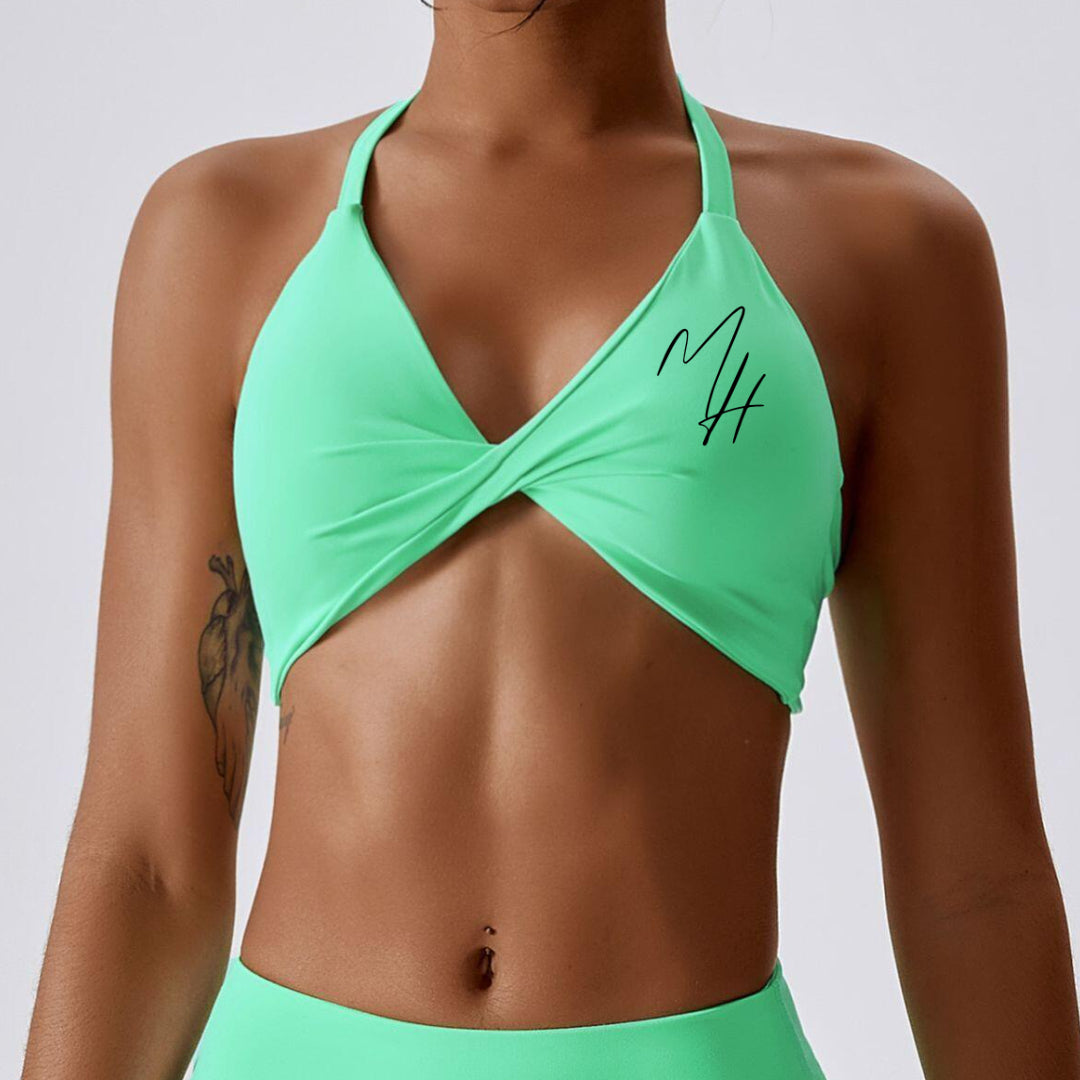 A photo of a woman wearing a stylish green 'BeYouAppleBottom' Crop Top paired with matching leggings, showcasing the epitome of style and functionality in activewear. The crop top features a flattering silhouette with the brand's iconic logo displayed on both front and back, while boasting padding for added support and a chic twist-hole design. This versatile ensemble transitions seamlessly from gym sessions to beach outings, embodying empowerment and self-expression.