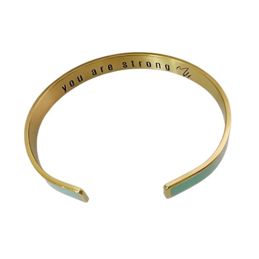 A gold-colored bangle bracelet with the inscription 'you are strong' on the inside, displayed against a white background.